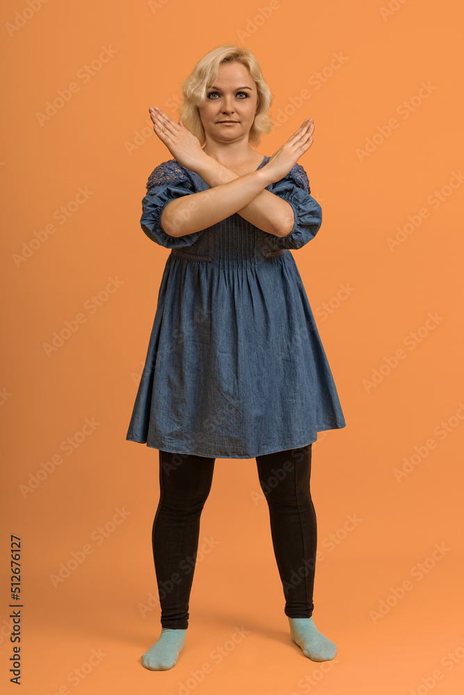 plus size blond woman in blue dress showing stop with crossed arms on color background plus size blond woman in blue dress showing stop with crossed arms on color background