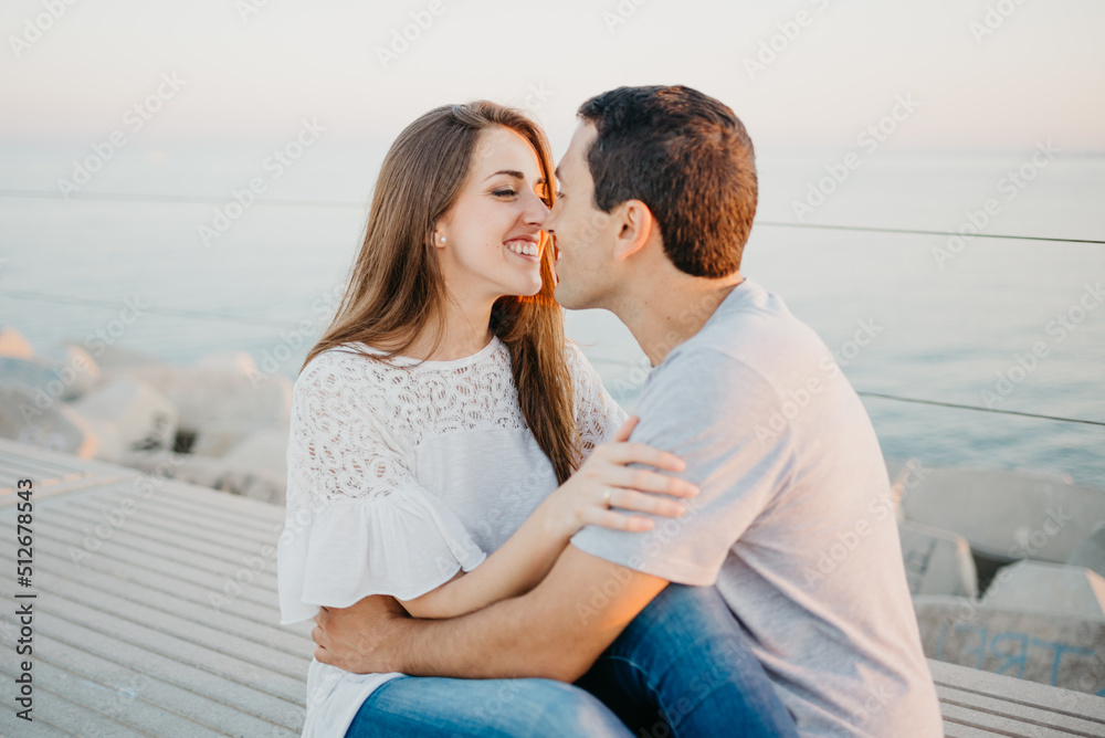 Hispanic man and a smiling brunette girl are sitting on a breakwater in Spain Hispanic man and a smiling brunette girl are sitting on a breakwater in Spain