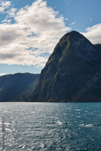 High mountains rise directly out of the water of Sognefjord  Norway on a beautiful and sunny day with clouds above the mountains. Summer feelings  vacation time.  