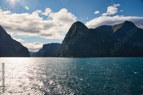 View from a ferry in Sognefjord, Norway with high mountains rising directly out of the water on a beautiful and sunny day with clouds above the mountains. Summer feelings, vacation time.   © Philipp