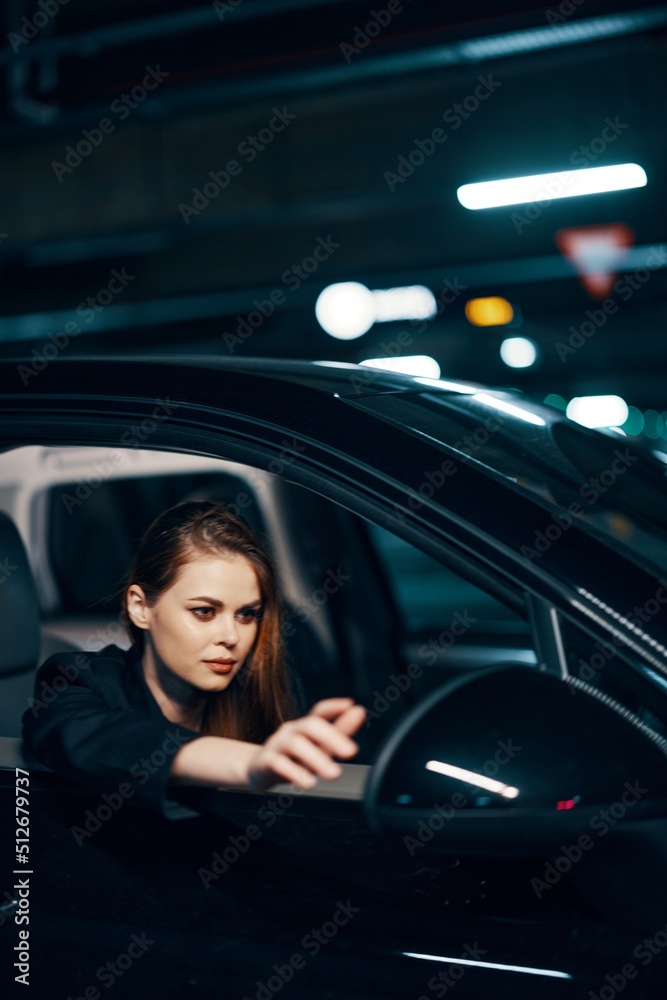 a vertical photo from the side, at night, of a woman sitting in a car and looking out of the window and reaching out with her hand to the side view mirror