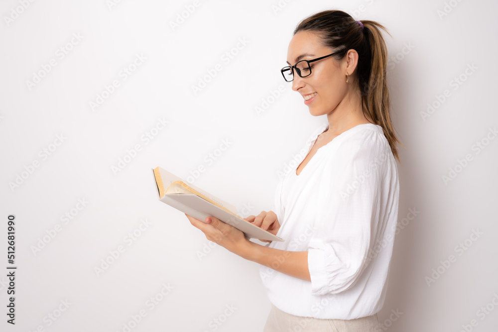 Young brunette woman wearing eyeglasses reading a book standing isolated over white background. Young brunette woman wearing eyeglasses reading a book standing isolated over white background.