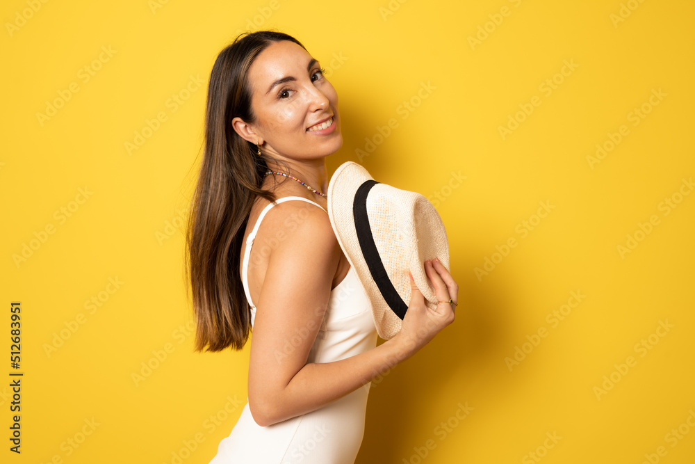 Young happy brunette woman in swimsuit holding straw hat standing isolated over yellow background. Summer holidays concept. Young happy brunette woman in swimsuit holding straw hat standing isolated over yellow background. Summer holidays concept.