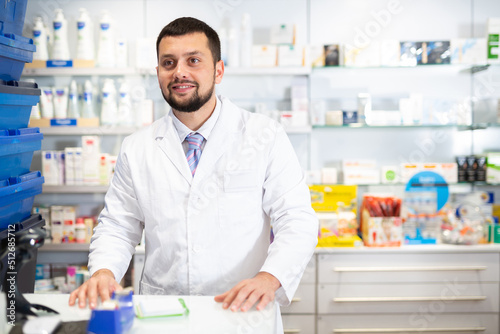 Portrait of smiling bearded caucasian man druggist standing at counter in pharmacy.