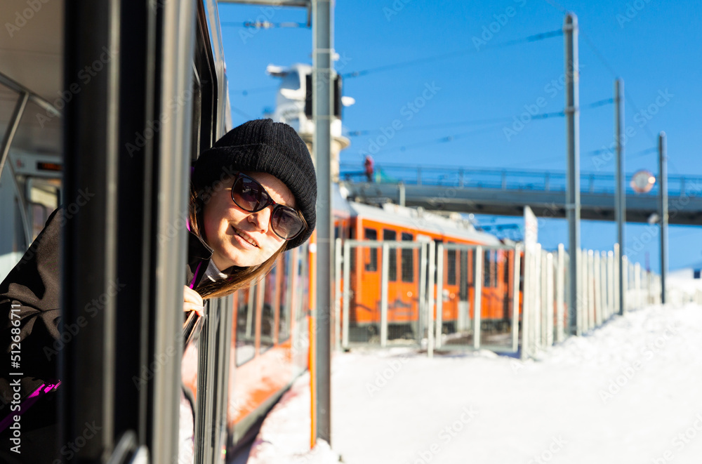 Obraz premium Happy woman in sunglasses sticking head out of window of mountain express train passing among snowy areas on sunny winter day 