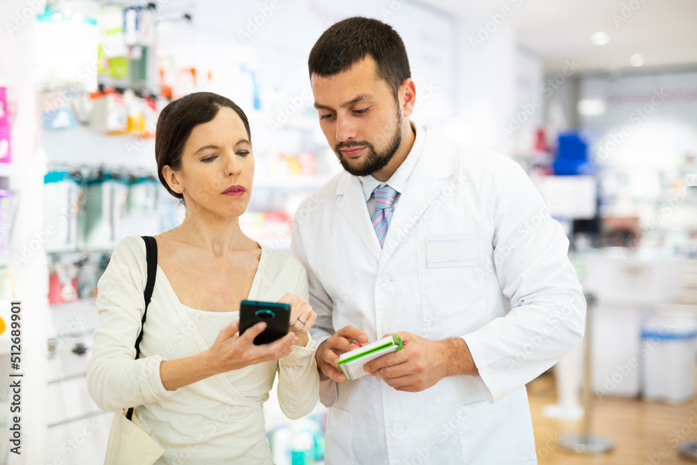 Woman using smartphone to show information about drug she looking for to male pharmacist.