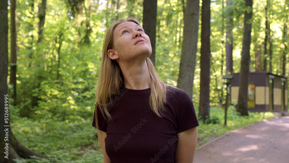 beautiful slender blonde walks through picturesque green forest at sunset or dawn. woman in black t-shirt looks up at birds or treetops. lady on walk in forest walks alone along paths. beautiful slender blonde walks through picturesque green forest at sunset or dawn. woman in black t-shirt looks up at birds or treetops. lady on walk in forest walks alone along paths.