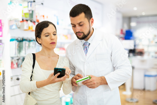 Woman using smartphone to show information about drug she looking for to male pharmacist.