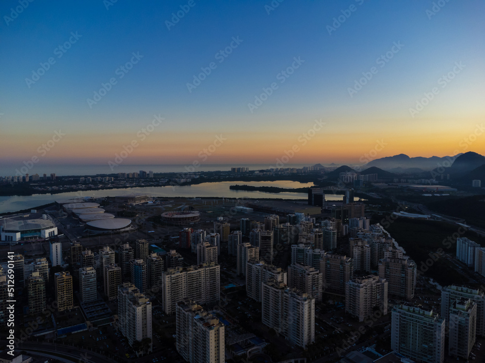 Fototapeta premium Aerial view of Jacarépagua lagoon in Rio de Janeiro, Brazil. Residential buildings and mountains around the lake. Barra da Tijuca beach in the background. Sunny day. Sunset. Drone photo