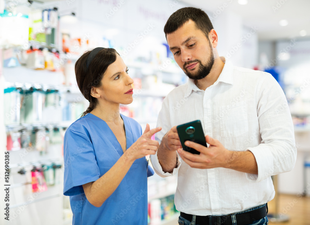 Man with smartphone having conversation with female apothecary and asking questions about drug. Pharmacist consulting man about medicine.