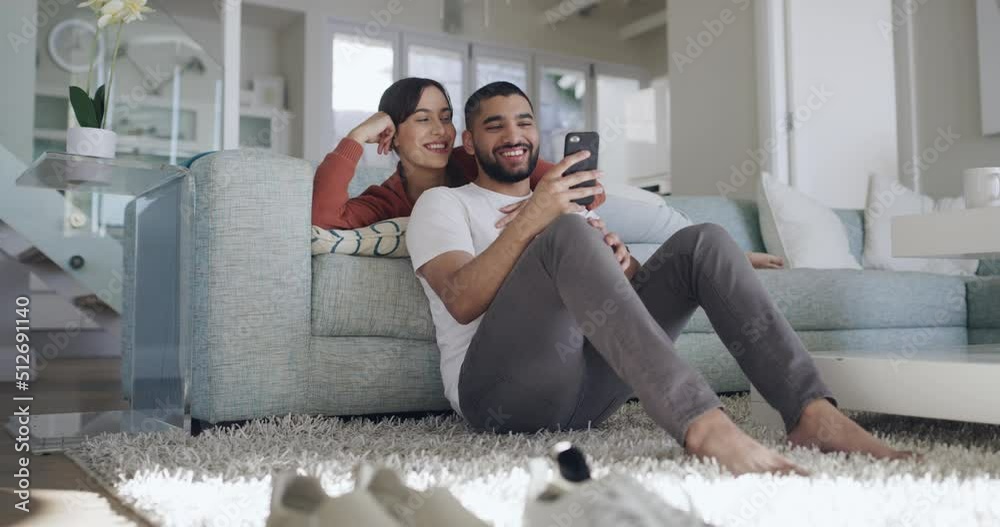 Happy and affectionate mixed race couple using a phone to text message, online chat or browse social media. In love boyfriend and girlfriend laughing while relaxing together on the sofa at home