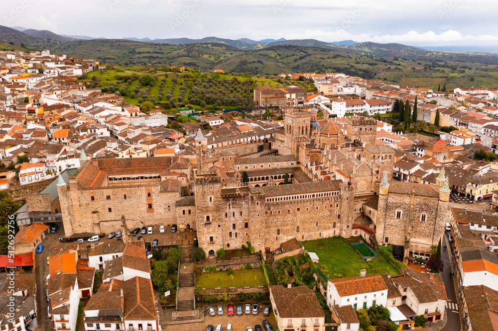 Gothic-Mudejar style building of Royal Monastery of Saint Mary in Spanish town of Guadalupe, located in green valley of province of Caceres overlooking brownish roofs of houses, as seen from drone..
