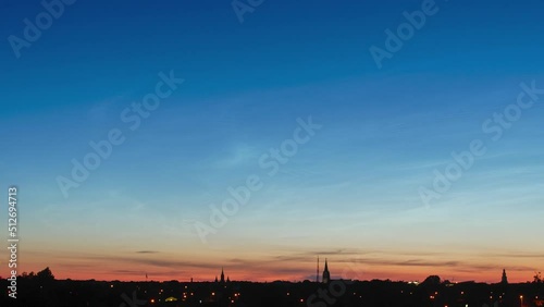 Beautiful time lapse of silvery (noctilucent, polar mesospheric) clouds glowing and shining in a summer evening, calm and tranquil scenic view after the sunset, cityscape, wide angle shot photo