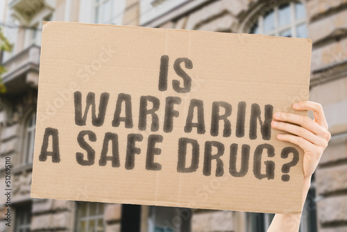 The question " Is warfarin a safe drug? " is on a banner in men's hands with blurred background. Safe. Safety. Formula. Secure. Science. Security. Poison. Caution. Danger. Protect. Carbon. Chemistry