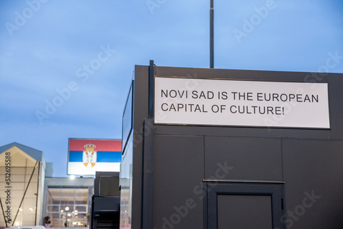 Selective blur on a sign indicating that Novi Sad is the European capital of culture for 2022 in English with a Serbian flag in back. it's an event aimed at promoting culture in European cities.....