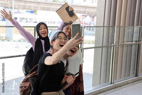 Four young attractive Asian group woman friends colleagues students talk walk discuss mingle outdoors backpack handphone outdoor notebook urban building cityscape taking selfie happy fun