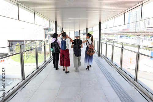 Four young attractive Asian group woman friends colleagues students talk walk discuss mingle outdoors backpack handphone outdoor notebook urban building cityscape at walkway bridge