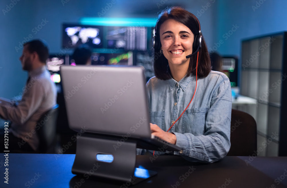 Smiling young female caucasian financial analyst working in the office with laptop and headset looking at camera. Smiling young female caucasian financial analyst working in the office with laptop and headset looking at camera.