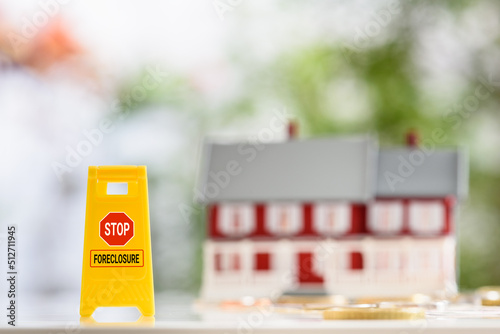 Strategies or ways to stop foreclosure or avoid foreclosure, mortgage relief, financial concept : Yellow sign board with the words STOP FORECLOSURE, a red-white two story house with coins on a table. photo