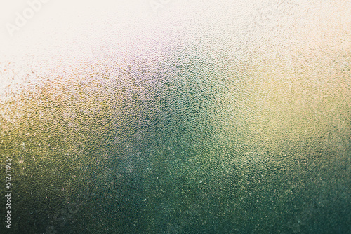 water droplets of humidity condensation on window glass seen from indoor with backyard bokeh in the background