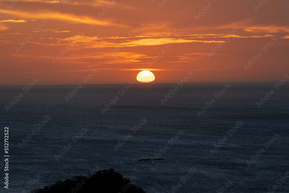 Beautiful view of an orange sunset in the midel of the Costa Rica Ocean, with a boat and pelicans 