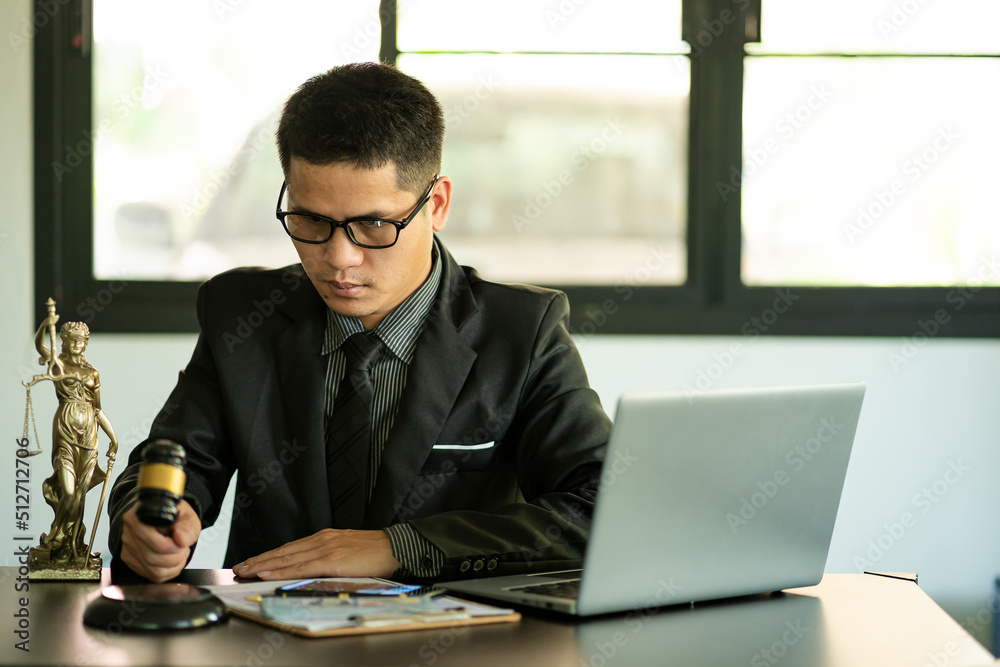 Middle aged Asian male lawyer working on laptop and legal contract documents in courtroom Judge's Hammer and Goddess Scales concept of legal counseling and services. Middle aged Asian male lawyer working on laptop and legal contract documents in courtroom Judge's Hammer and Goddess Scales concept of legal counseling and services.