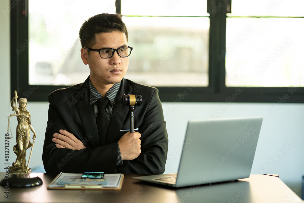 Middle aged Asian male lawyer working on laptop and legal contract documents in courtroom Judge's Hammer and Goddess Scales concept of legal counseling and services. Middle aged Asian male lawyer working on laptop and legal contract documents in courtroom Judge's Hammer and Goddess Scales concept of legal counseling and services.