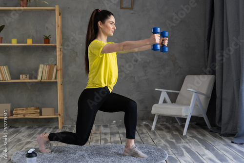 Lunging forward. Sportswoman lunging forward with blue dumbbells at home. Sport, healthy lifestyle