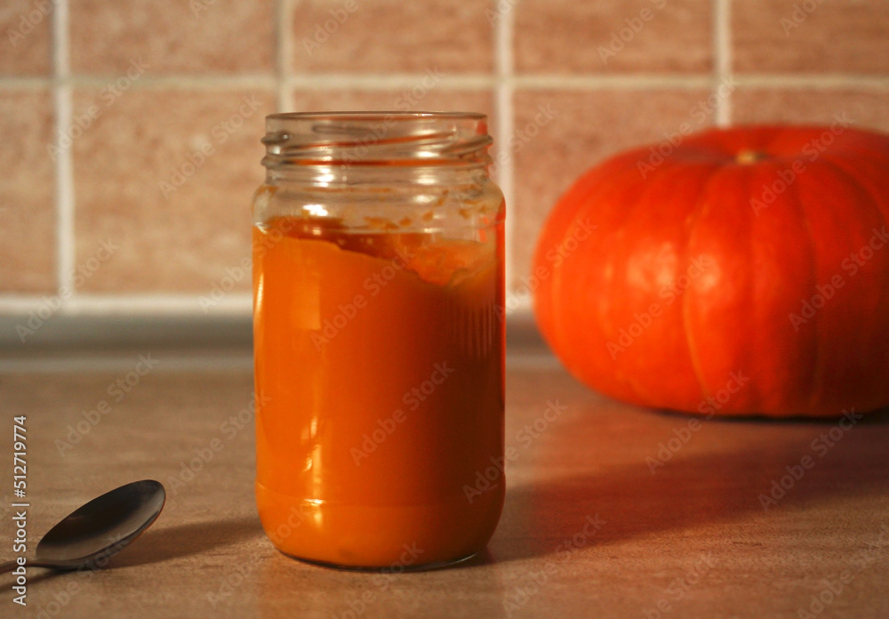 baby pumpkin puree in a glass jar with a spoon and fresh pumpkin