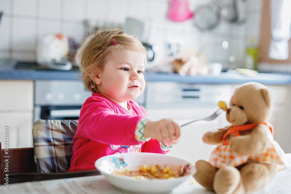 Adorable baby girl eating from fork vegetables and pasta. food, child, feeding and development concept. Cute toddler, daughter with spoon sitting in highchair and learning to eat by itself. Adorable baby girl eating from fork vegetables and pasta. food, child, feeding and development concept. Cute toddler, daughter with spoon sitting in highchair and learning to eat by itself.