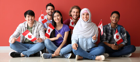 Group of students with Canadian flags sitting near red wall