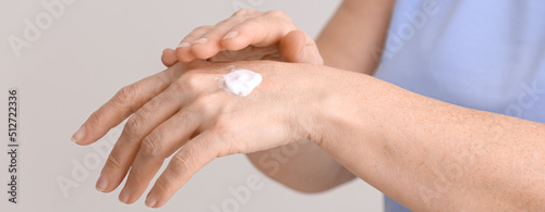 Mature woman applying hand cream against grey background  closeup