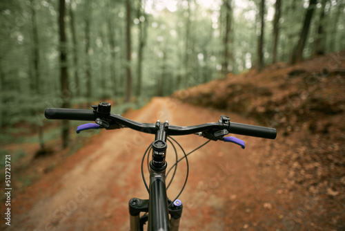 Mountain bike handlebar viewed from the first-person perspective. visible bicycle frame and bicycle accessories on the handlebar and the forest trai. Concept of spending time outdoors while bikeriding