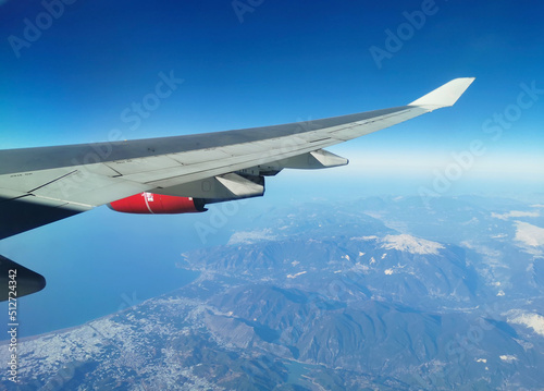 View from the porthole on the wing of an airplane with a red aircraft engine flying to Cyprus in the morning over beautiful mountains with snowy peaks.