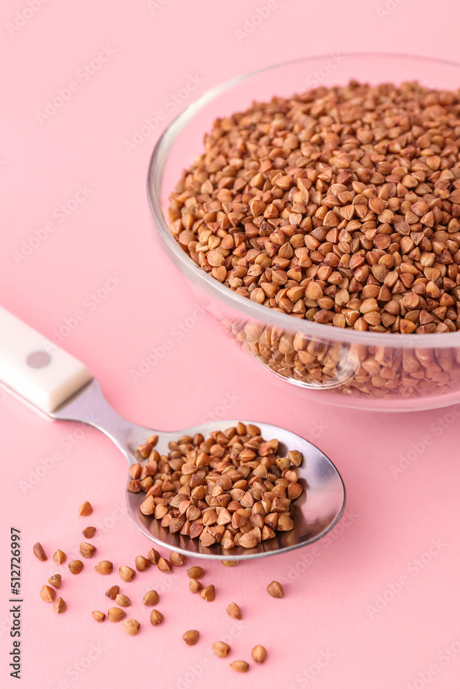 Glass bowl and spoon with buckwheat grains on pink background Glass bowl and spoon with buckwheat grains on pink background