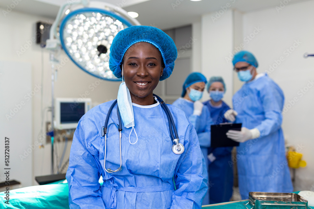 Portrait of happy African American woman surgeon standing in operating room, ready to work on a patient. Female medical worker in surgical uniform in operation theater.