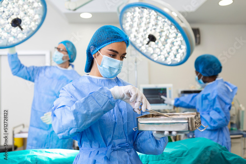 Female surgeon in surgical uniform taking surgical instruments at operating room. Young woman doctor in hospital operation theater photo