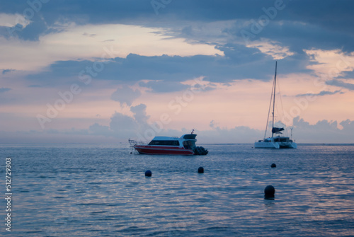 Beautiful sunrise on calm sea with smooth waves, colorful light sky with fluffy clouds, yacht and boat on horizon. Marine landscape on early morning in indonesian ocean, bright vacation in asia.