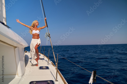 Beautiful young blond woman in bikini standing on catamaran at sunny summer day © Anatoly Repin