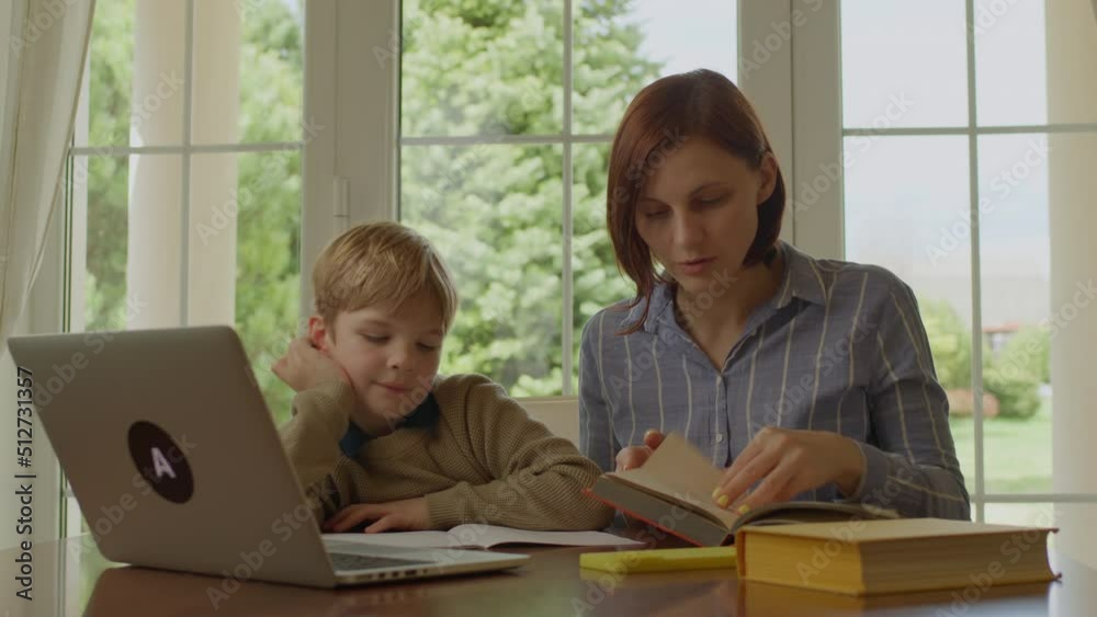 30s mother helping her son with online homework. Family learning together using laptop. Home schooling.