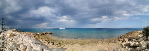 Panorama. The stone coast of the Mediterranean Sea, a white pleasure ship in the sea against a dramatic sky. with clouds.