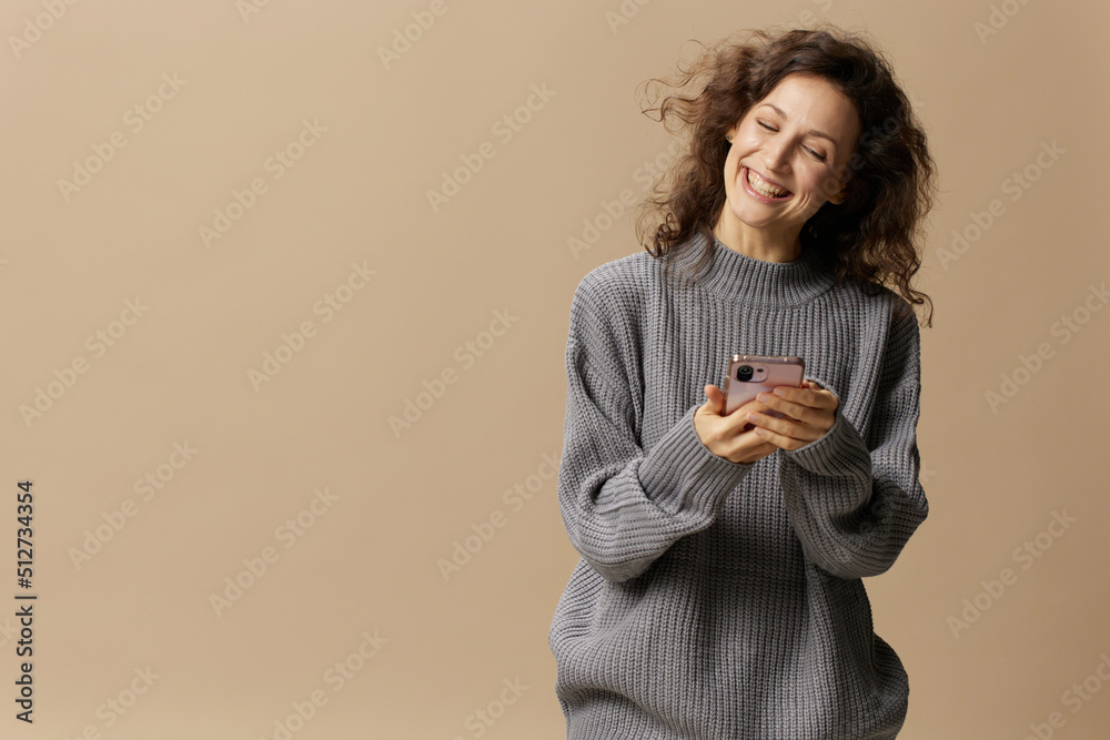 Lovely happy curly beautiful female in gray casual sweater chatting with boyfriend posing isolated on over beige pastel background. Social media, network, distance communication concept. Copy space Lovely happy curly beautiful female in gray casual sweater chatting with boyfriend posing isolated on over beige pastel background. Social media, network, distance communication concept. Copy space