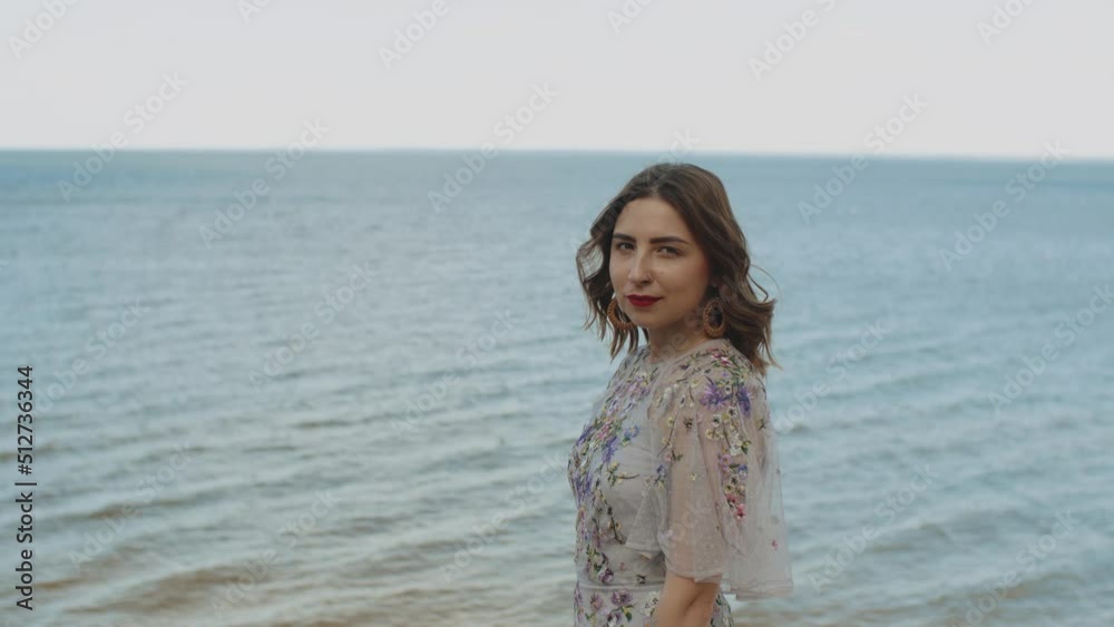 Portrait of attractive woman with red lips and curly hair looking at camera, medium shot, slow motion. blue sea with waves and blue sky in the background. Portrait of attractive woman with red lips and curly hair looking at camera, medium shot, slow motion. blue sea with waves and blue sky in the background.