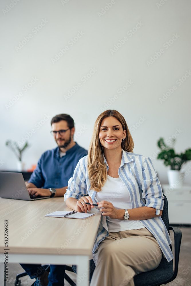 Portrait of a smiling blonde woman, posing while her male colleague working in the background. Portrait of a smiling blonde woman, posing while her male colleague working in the background.