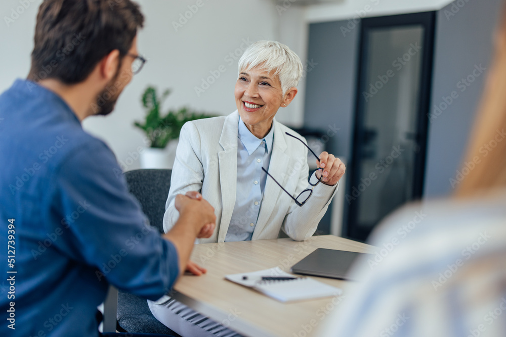 A smiling female insurance agent finished the meeting, shaking hands with a male client. A smiling female insurance agent finished the meeting, shaking hands with a male client.