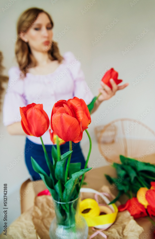 A young woman is packing a festive bouquet in wrapping paper. The florist makes an assembly with red tulips in the workshop. A woman at work, in a small business or hobby. A young woman is packing a festive bouquet in wrapping paper. The florist makes an assembly with red tulips in the workshop. A woman at work, in a small business or hobby.