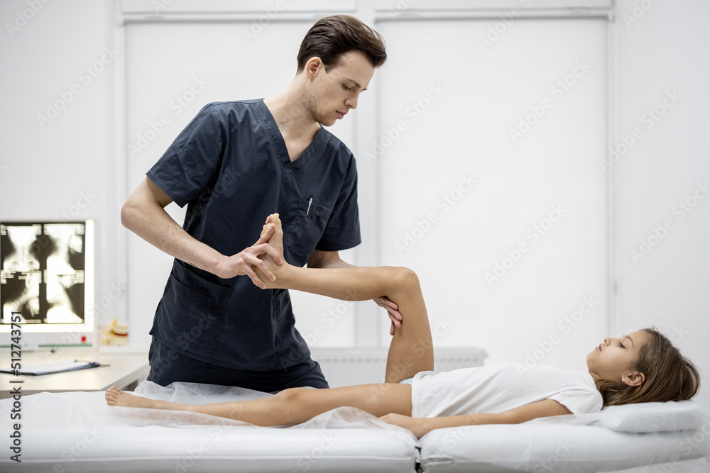 Pediatric orthopedist examines limbs and joints of 10-aged girl on couch in the medical office. Concept of pediatrics and examination for a healthy musculoskeletal child's system Pediatric orthopedist examines limbs and joints of 10-aged girl on couch in the medical office. Concept of pediatrics and examination for a healthy musculoskeletal child's system
