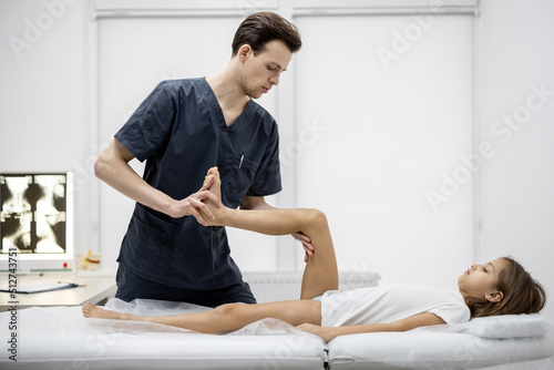Pediatric orthopedist examines limbs and joints of 10-aged girl on couch in the medical office. Concept of pediatrics and examination for a healthy musculoskeletal child's system
