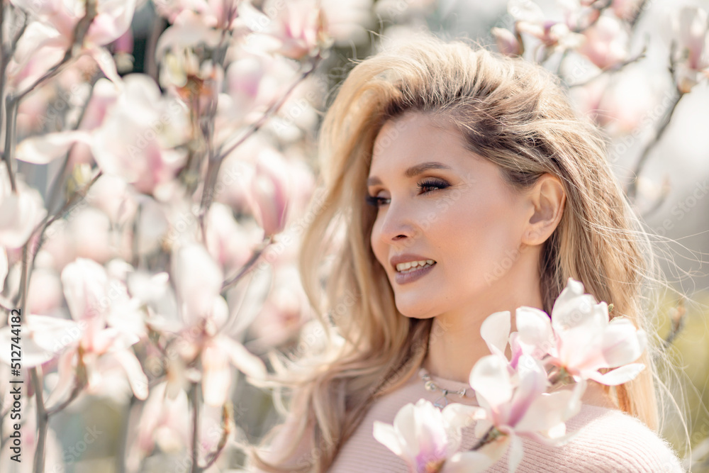 Portrait of a beautiful happy middle aged woman enjoying the smell in a blooming spring garden. Beautiful magnolia bushes, large flowers. Portrait of a beautiful happy middle aged woman enjoying the smell in a blooming spring garden. Beautiful magnolia bushes, large flowers.