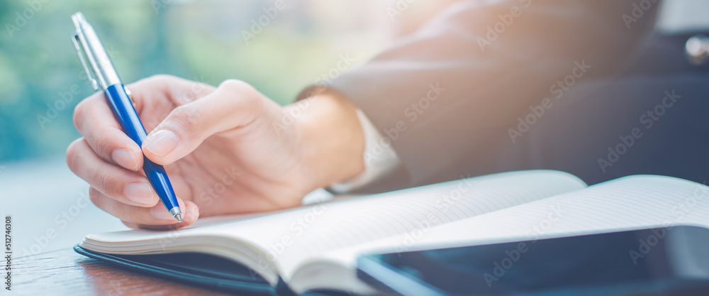 Woman hand writing on a notepad with a pen in the office.
